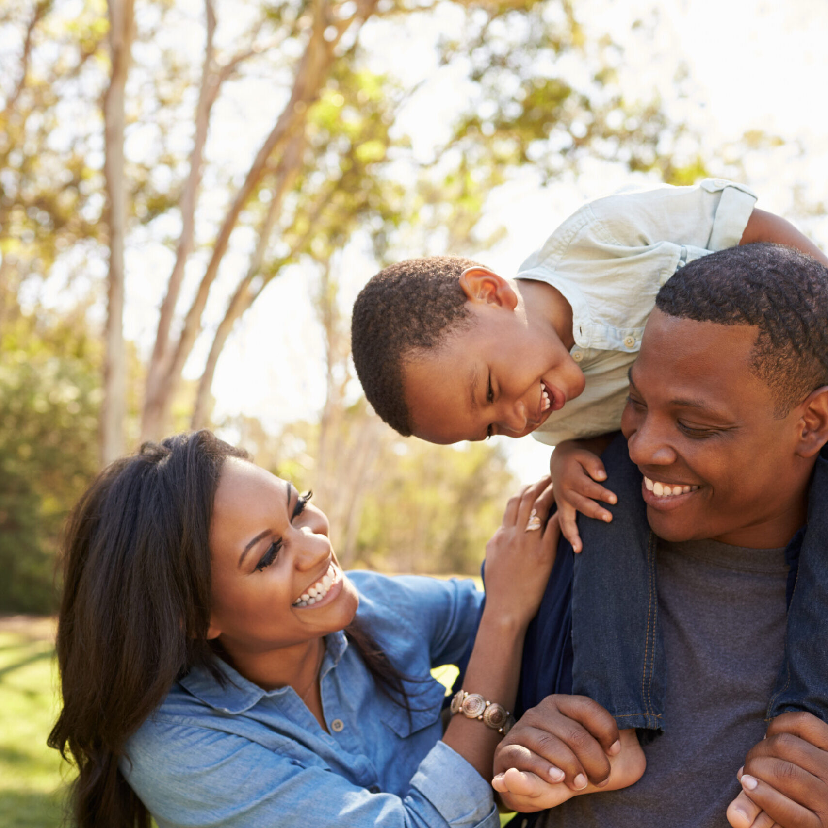 Parents,Carrying,Son,On,Shoulders,As,They,Walk,In,Park