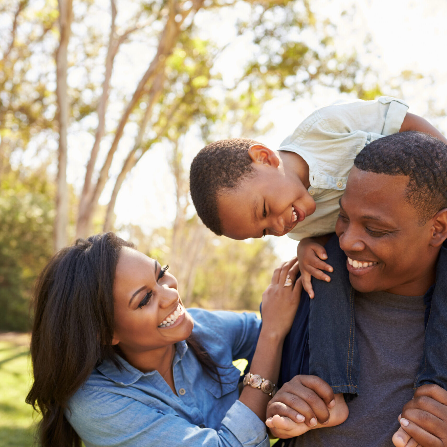 Parents,Carrying,Son,On,Shoulders,As,They,Walk,In,Park